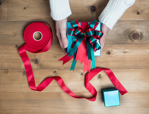 Creative hobby. Woman's hands wrap christmas holiday handmade present in craft paper with twine ribbon. Making bow gift box, decorated with cute object on wooden table, top view.flat lay composition