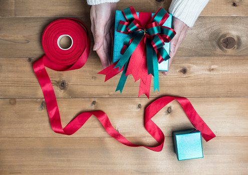 Creative hobby. Woman's hands wrap christmas holiday handmade present in craft paper with twine ribbon. Making bow gift box, decorated with cute object on wooden table, top view.flat lay composition