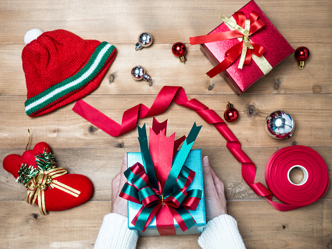 Creative hobby. Woman's hands wrap christmas holiday handmade present in craft paper with twine ribbon. Making bow gift box, decorated with cute object on wooden table, top view.flat lay composition