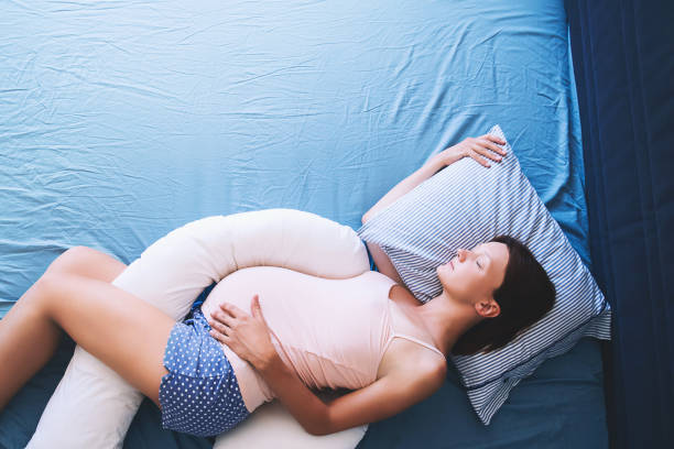 Beautiful pregnant woman relaxing or sleeping with tummy supporting pillow at bed. Beautiful pregnant woman relaxing or sleeping with tummy supporting pillow at bed. Young mother waiting of a baby. Concept of pregnancy, maternity, health care, gynecology, medicine. night hospital bed stock pictures, royalty-free photos & images