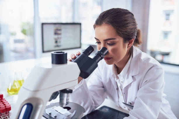 State of the art science equipment Shot of a cheerful young female scientist looking through the lens of a microscope while being seated inside of a laboratory biochemist stock pictures, royalty-free photos & images