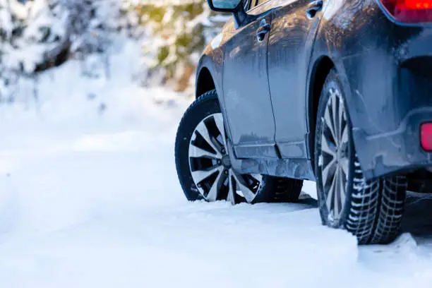 Photo of Winter tires. Black SUV car rear view on snowy forest road. Winter conditions.