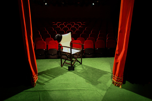 Director's chair on stage, in front of empty seats and in between curtains