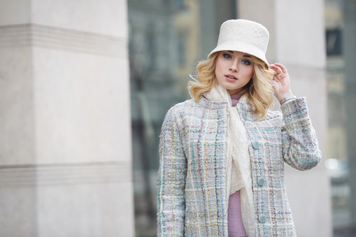Portrait of a beautiful stylish blonde woman in a coat and hat on a city street.