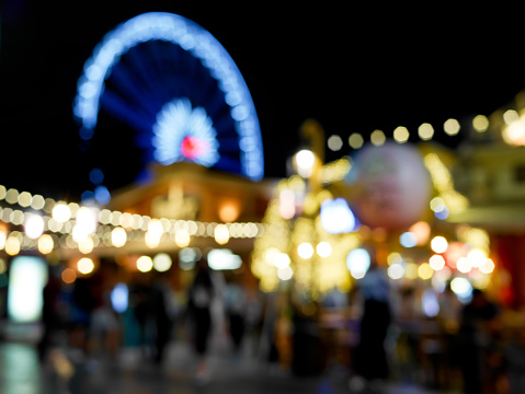 Blurred ferris wheel, restaurant and a lot of people in amusement park. Abstract bokeh background.