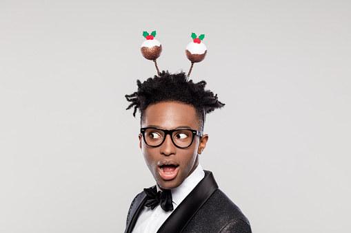 Funny portrait of surprised elegant young man wearing Christmas headband. Man wearing jacket and bow tie gasping against white background.