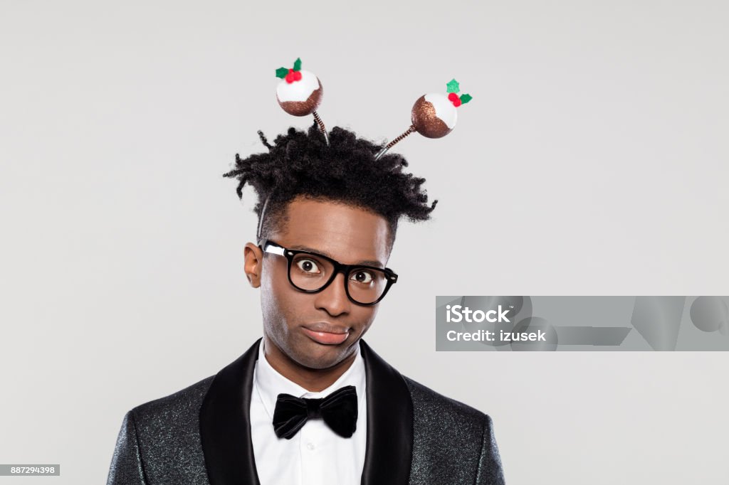 Portrait of displeased elegant man wearing christmas headband Portrait of disappointed elegant young man wearing Christmas headband. Man wearing jacket and bow tie standing against white background. Christmas Stock Photo