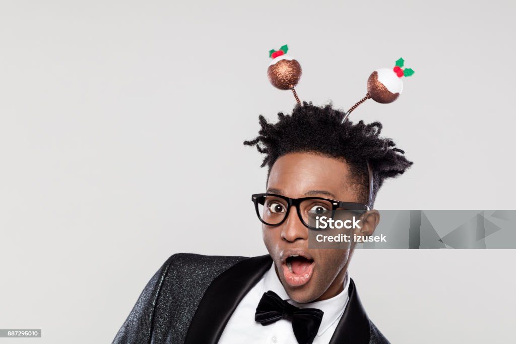 Funny portrait of excited elegant man wearing christmas headband Funny portrait of happy elegant young man wearing Christmas headband. Man wearing jacket and bow tie laughing against white background. Christmas Stock Photo
