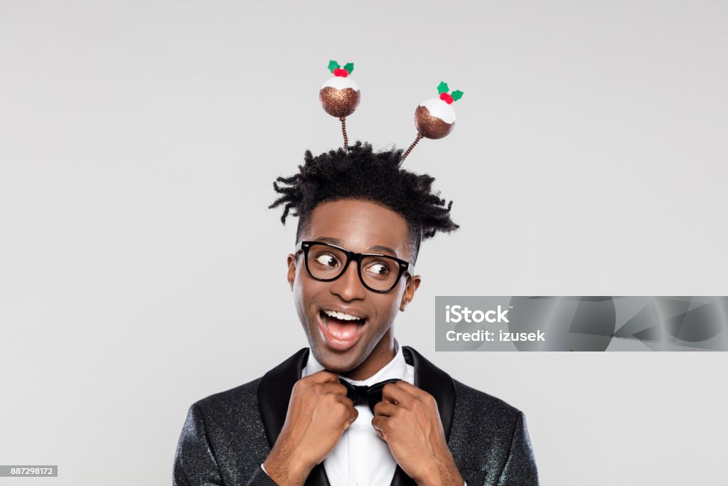 Funny portrait of excited elegant man wearing christmas headband Funny portrait of happy elegant young man wearing Christmas headband. Man wearing jacket and bow tie laughing against white background. Christmas Stock Photo