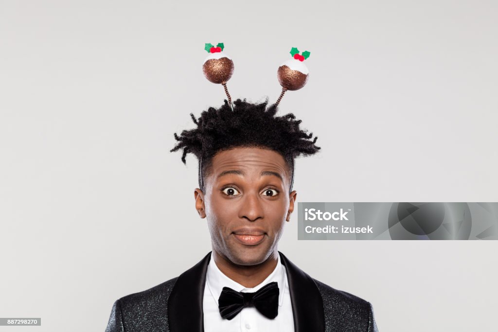 Funny portrait of surprised elegant man wearing christmas headband Funny portrait of happy elegant young man wearing Christmas headband. Man wearing jacket and bow tie staring at the camera against white background. African Ethnicity Stock Photo
