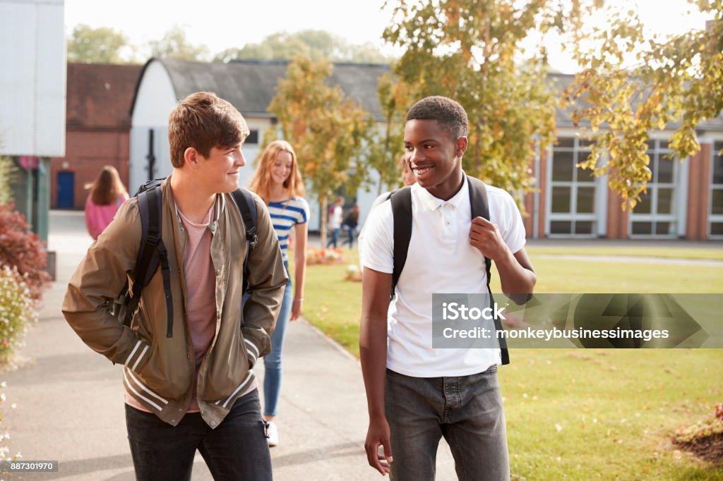 Alunos do sexo masculino adolescentes andando pelo Campus da faculdade juntos - Foto de stock de Falar royalty-free