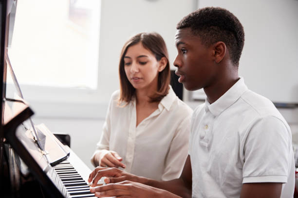 Male Pupil With Teacher Playing Piano In Music Lesson Male Pupil With Teacher Playing Piano In Music Lesson music theory stock pictures, royalty-free photos & images