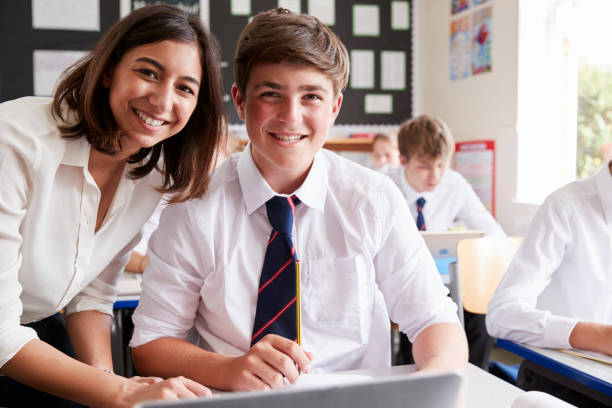 istock Portrait Of Teacher Helping Pupil Using Computer In Classroom 887303062