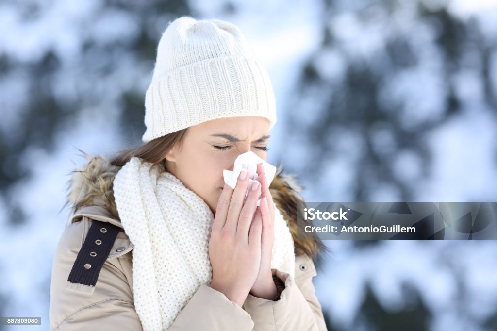 Woman blowing in a tissue in a cold snowy winter Woman blowing in a tissue in a cold winter with a snowy mountain in the background Winter Stock Photo