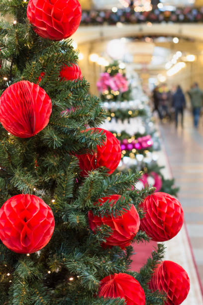 Christmas tree with holiday red balls and lights with copy space on blurred bokeh background in mall. Close up.
