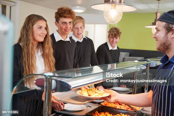 Photo libre de droit de Teenage Étudiants Desservis Repas En Cantine Scolaire banque d'images et plus d'images libres de droit de Cantine