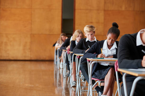 Teenage Students In Uniform Sitting Examination In School Hall Teenage Students In Uniform Sitting Examination In School Hall educational exam stock pictures, royalty-free photos & images