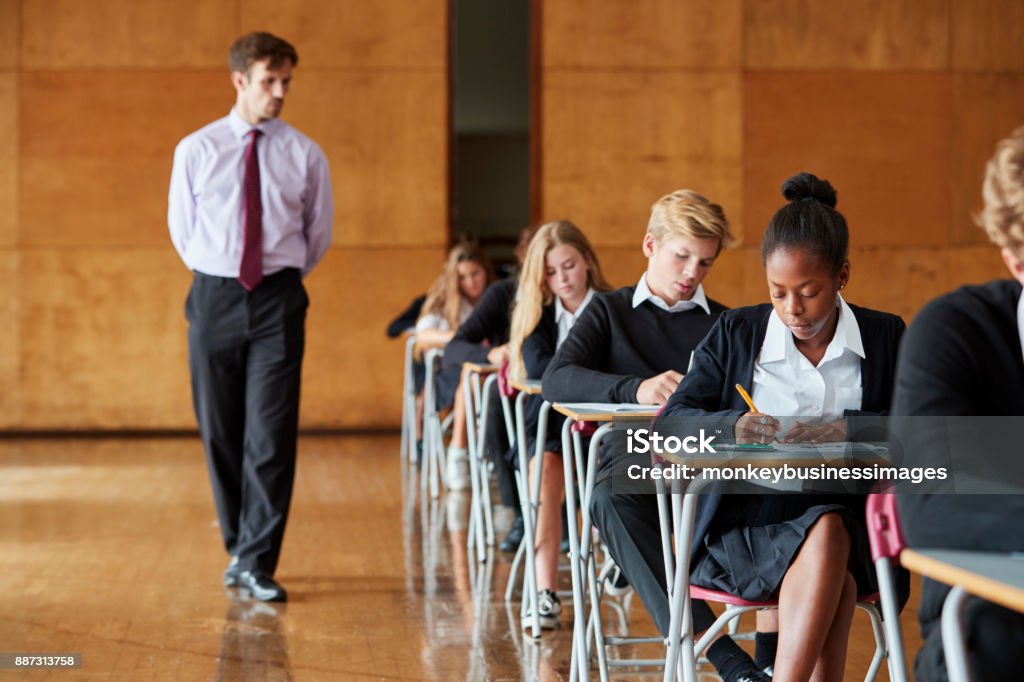 Studenti adolescenti seduti esame con insegnante vegliante - Foto stock royalty-free di Esame