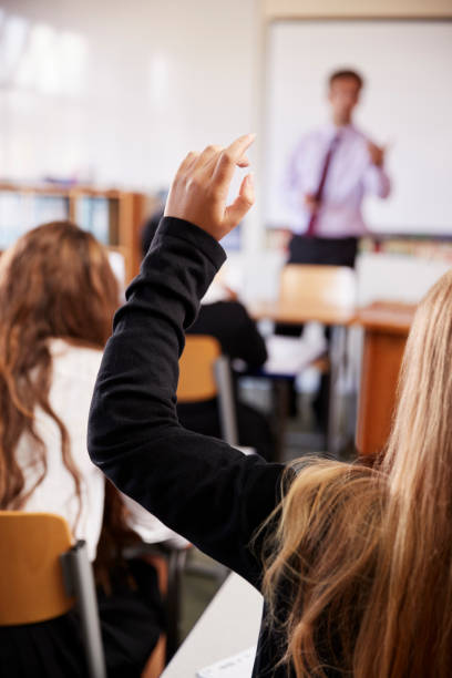 istock Female Student Raising Hand To Ask Question In Classroom 887318058