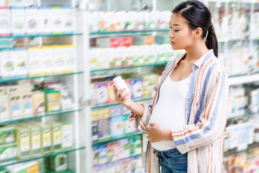 young pregnant woman holding container with medication in drugstore