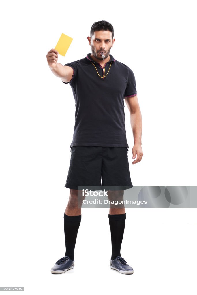 Infringement of Soccer Rules Full length portrait of confident mixed race soccer referee showing yellow card and blowing whistle while standing against white background Referee Stock Photo