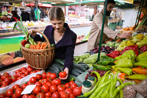 Young woman buying vegetables at farmer's market stall.