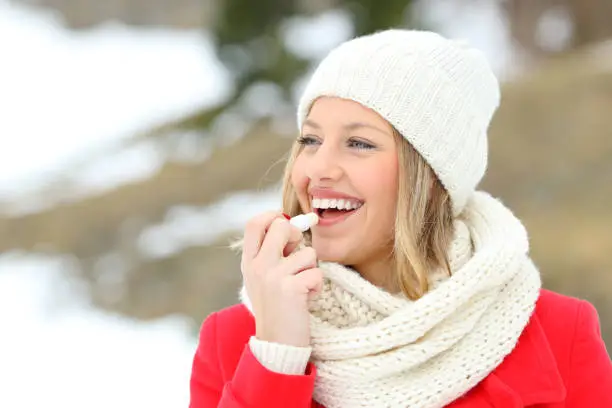 Girl protecting lips with lip balm in winter with a snowy mountain in the background