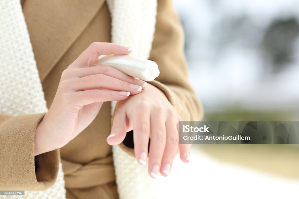 Woman hydrating hands with moisturizer cream Close up of a woman hydrating hands with moisturizer cream in winter with a snowy mountain in the background Dry Stock Photo