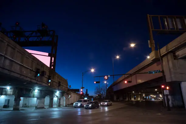 Photo of Gritty dark Chicago city street intersection under industrial train bridge viaduct tunnel and highway with CTA bus stops at night.