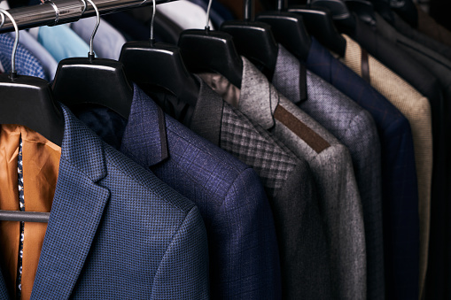 Mens suits in different colors hanging on hanger in a retail clothes store, close-up