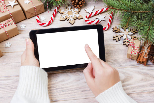 istock Christmas background: female hands uses opened tablet with copy space on rustic wooden table covered with Christmas decoration. top view, flat lay 887389320
