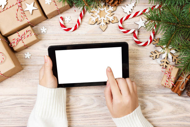 istock Christmas background: female hands uses opened tablet with copy space on rustic wooden table covered with Christmas decoration. top view, flat lay 887389322