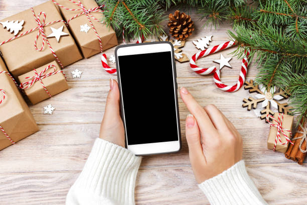 istock Christmas background: female hands writing in opened smartphone with copy space on rustic wooden table covered with Christmas decoration. top view, flat lay 887389336