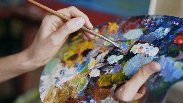 Close up of woman's hand mix paints with brush in palette in art-class Close up of woman's hand mix paints with brush in palette in art-class indoors oil painting photos stock pictures, royalty-free photos & images
