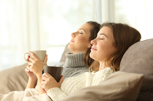 Side view portrait of two roommates relaxing in winter sitting on a sofa in the living room in a house interior