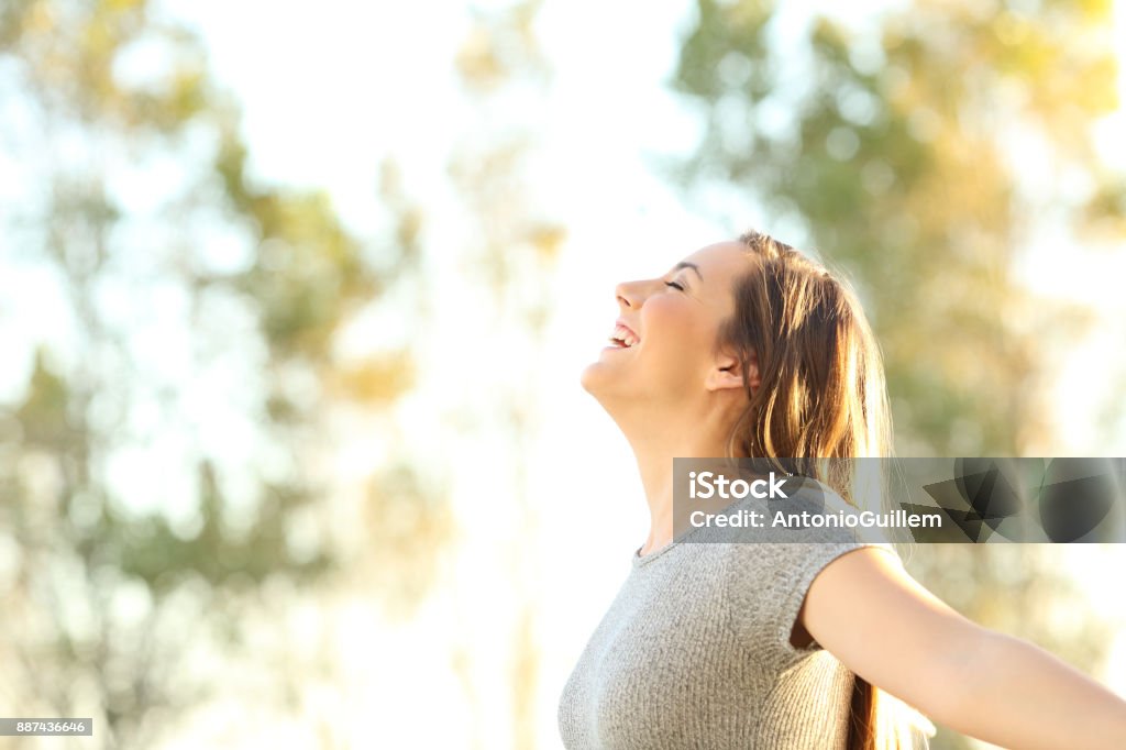 Woman breathing fresh air outdoors in summer Side view portrait of a woman breathing fresh air outdoors in summer with trees and sky in the background Women Stock Photo