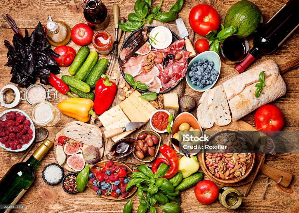 Top view table full of food Top view table full of food. Italian antipasti wine snacks set. Cheese variety, nuts, Mediterranean olives, sauces, Prosciutto di Parma or jamon, tomatoes, vegatables and berries and wine over wooden background Healthy Eating Stock Photo