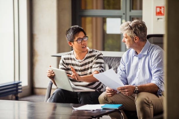 Sharing His Business Plan Two business people sitting on a sofa together in deep discussion with a laptop in front of them male chinese student stock pictures, royalty-free photos & images