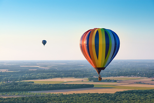 Aerial view of multicolored hot air balloons flying over a forest on evening lighting