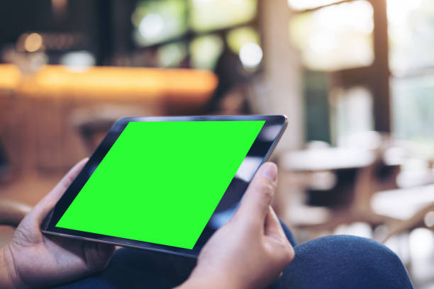 istock Mockup image of woman's hands holding black tablet pc with blank green screen on thigh with concrete floor background in modern cafe 887452134