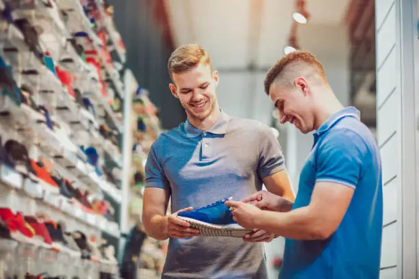 Photo of Two man deciding on new sports shoes in sports store