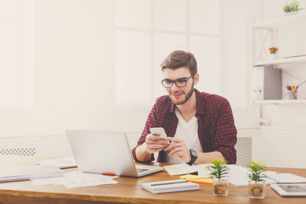 istock Young happy businessman in office using cell phone by the laptop 887464912