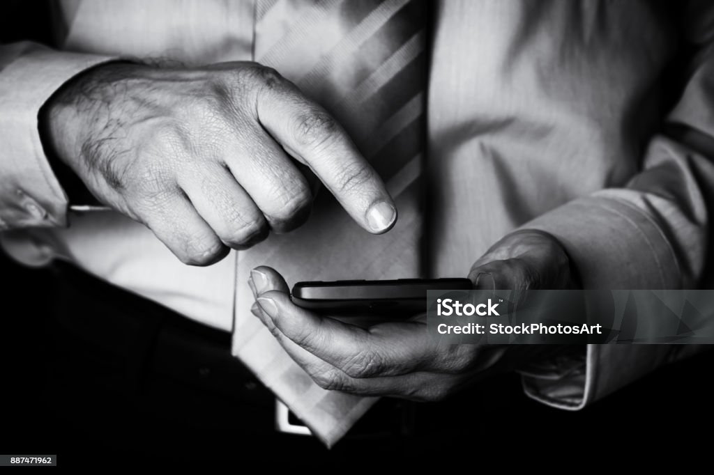 Man holding and touching screen or display with finger of a mobile phone, cell phone or smartphone. Man holding and touching screen or display with finger of a mobile phone, cell phone or smartphone. Male businessman typing a message or browsing the internet for apps on wireless digital device Black And White Stock Photo