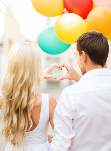 summer holidays, celebration and dating concept - couple with colorful balloons making heart shape in the city