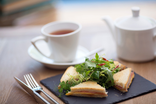 a variety of club sandwiches served in a white plate with a cup of hot tea in a pot and cup. Tasty