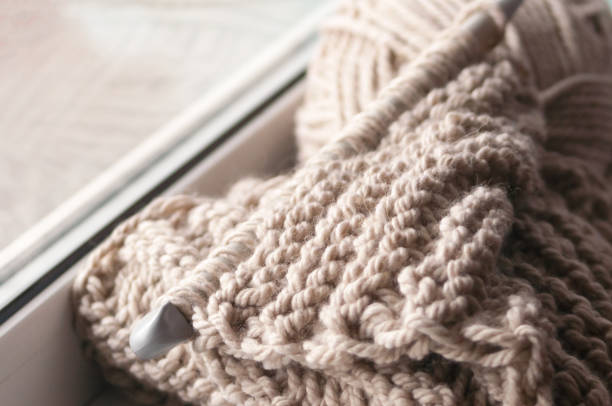 istock A knitted scarf with a thick thread on thick beige knitting needles. Close-up with blur. 887491108