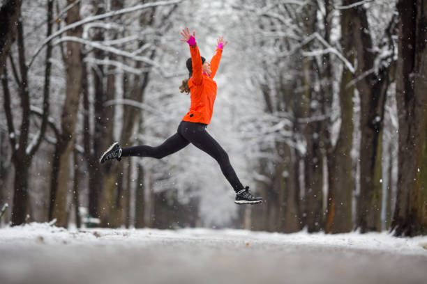 ¡salta! -mujer de vista lado saltando para la alegría en invierno - sports clothing practicing success vitality fotografías e imágenes de stock