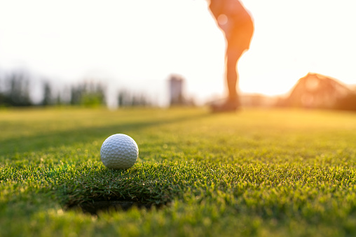 Golfista mujer asiática pone la pelota de golf en el campo de golf verde en sol establecer tiempo de noche, seleccione foco. Saludable y el concepto de estilo de vida. photo