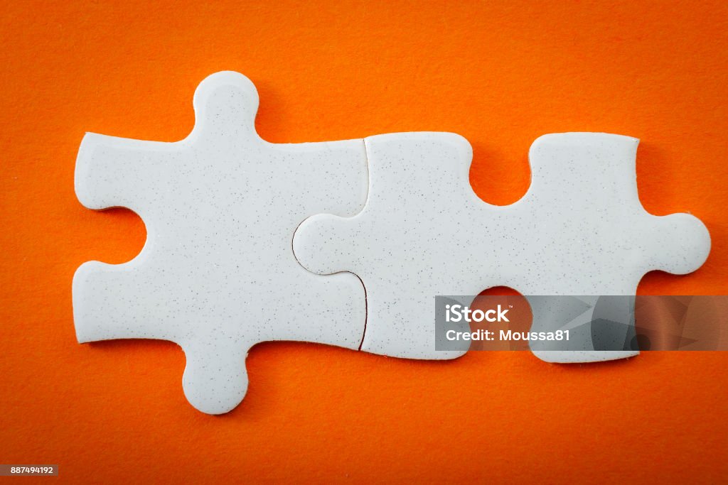 Business concept, connected puzzle pieces on orange background with copyspace The whole is greater than the sum of its parts concept with two blank puzzle pieces interlocked with copy space for text on the empty puzzles that interlock to illustrate 2 ideas that work together Bridging The Gap Stock Photo