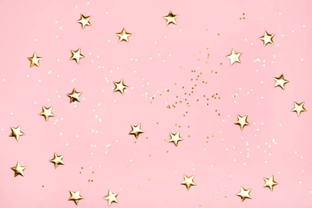 Photo of Golden stars glitter on pink background.